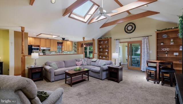 living area featuring a skylight, a ceiling fan, light colored carpet, high vaulted ceiling, and beamed ceiling