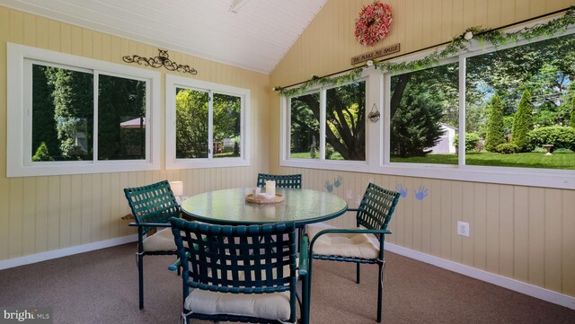 sunroom / solarium featuring carpet flooring, lofted ceiling, wood walls, and baseboards