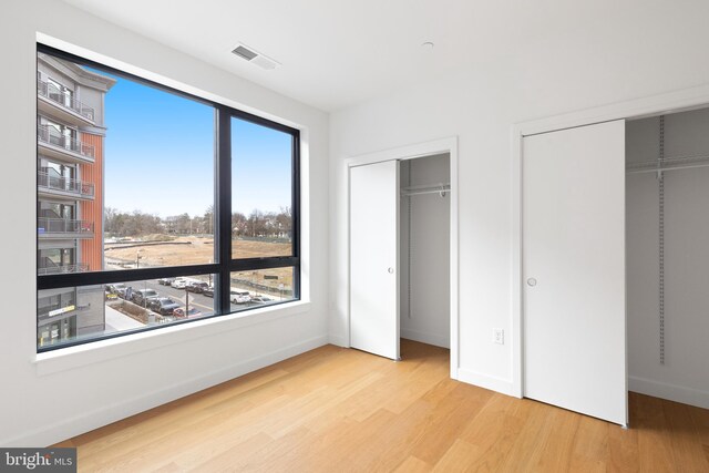 7175 12th St NW Unit 506, Washington, DC 20011 - unfurnished bedroom with baseboards, multiple closets, visible vents, and wood finished floors