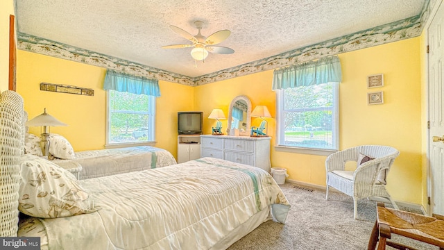 bedroom with a ceiling fan, a textured ceiling, visible vents, baseboards, and carpet flooring