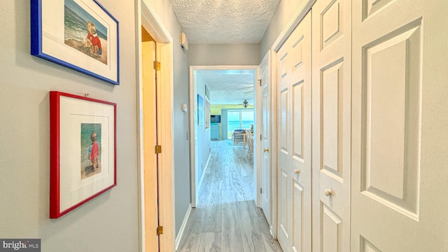 corridor with a textured ceiling, baseboards, and light wood-style floors