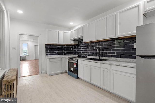 kitchen with under cabinet range hood, radiator heating unit, appliances with stainless steel finishes, and a sink
