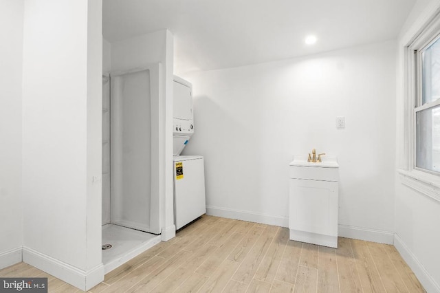 clothes washing area featuring laundry area, baseboards, light wood-type flooring, a sink, and stacked washer / drying machine