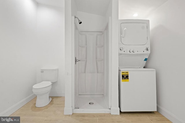 full bathroom featuring baseboards, stacked washer and dryer, wood finished floors, and a shower stall