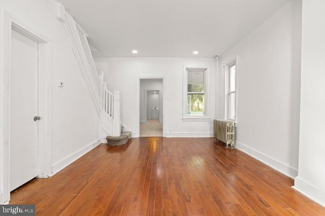 unfurnished living room featuring stairs, recessed lighting, hardwood / wood-style flooring, and radiator