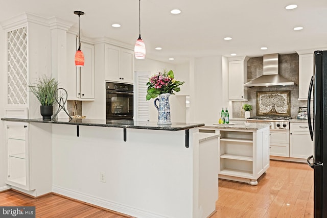 1716 Saddle Ridge Ct, Vienna, VA 22182 - kitchen with wall chimney range hood, oven, freestanding refrigerator, light wood finished floors, and a peninsula