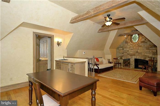 interior space with light wood-style floors, a sink, a stone fireplace, and vaulted ceiling with beams
