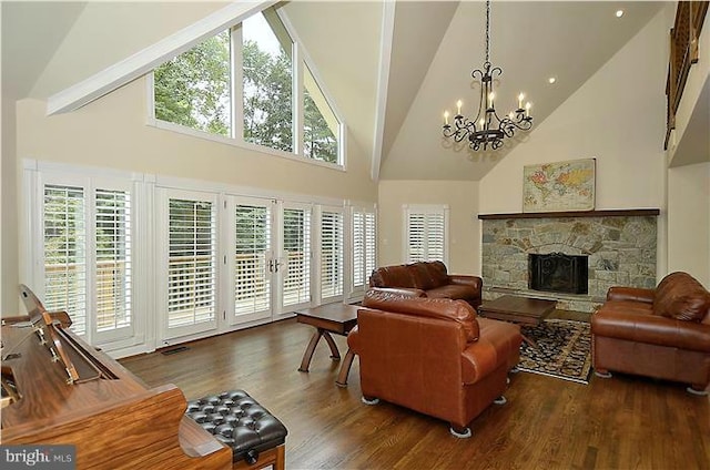 living room featuring wood finished floors, a stone fireplace, high vaulted ceiling, plenty of natural light, and a notable chandelier