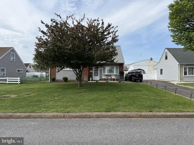 view of property hidden behind natural elements with brick siding, fence, and a front yard