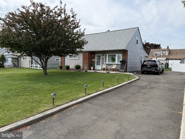 view of front of house with fence, a front yard, brick siding, a shingled roof, and driveway