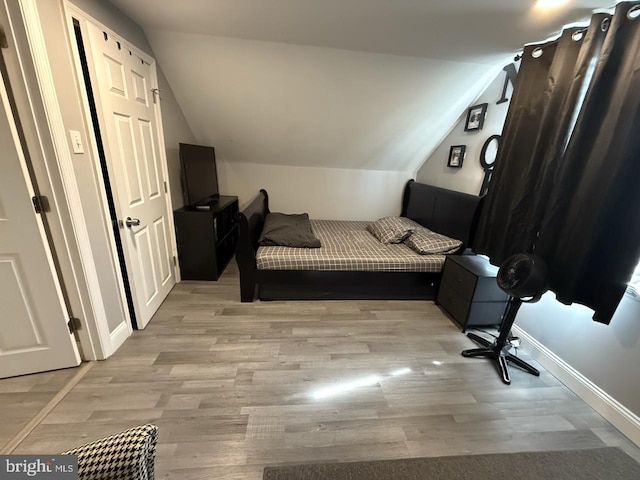 bedroom featuring light wood-style floors, baseboards, and lofted ceiling