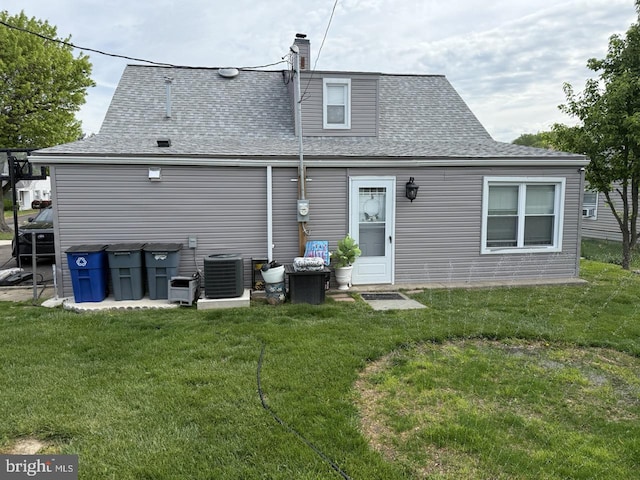 rear view of house with a lawn, central AC unit, and a shingled roof