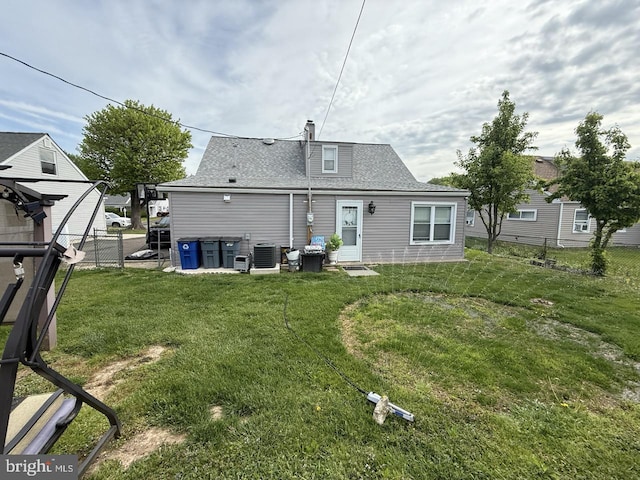 back of house with central air condition unit, a shingled roof, fence, and a yard