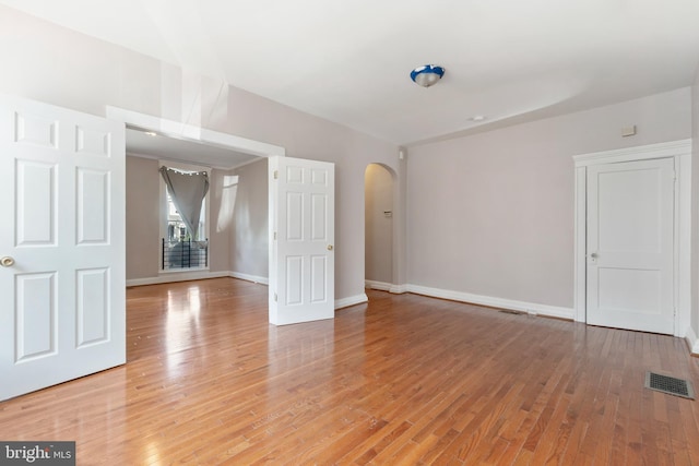 empty room featuring arched walkways, baseboards, visible vents, and light wood finished floors