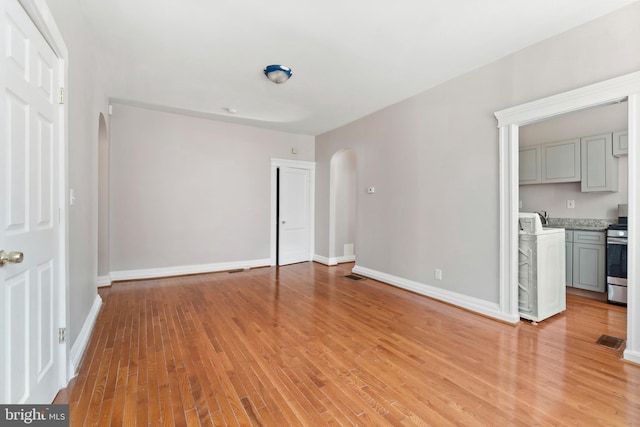 unfurnished living room featuring visible vents, a sink, baseboards, arched walkways, and light wood-style flooring