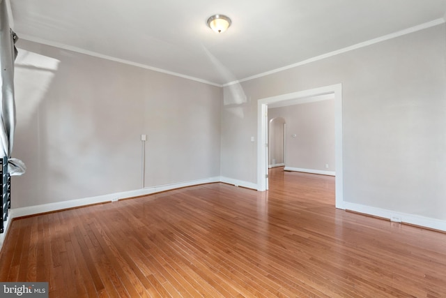 unfurnished room with arched walkways, baseboards, ornamental molding, and light wood-style floors