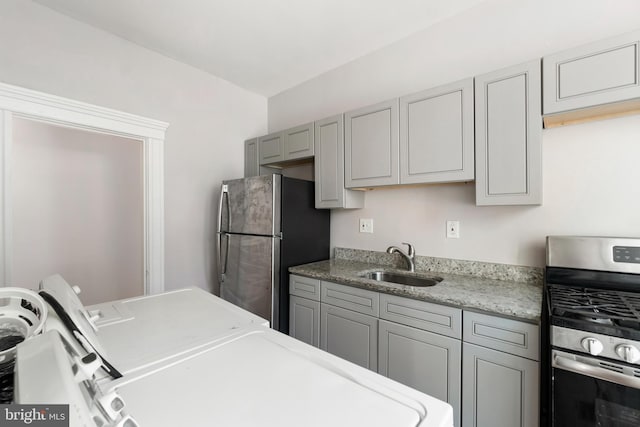 kitchen with independent washer and dryer, gray cabinets, light stone counters, a sink, and appliances with stainless steel finishes