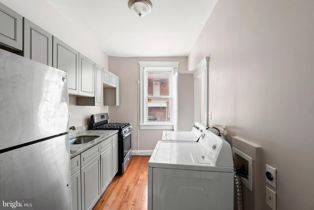 kitchen with a sink, appliances with stainless steel finishes, washing machine and dryer, and gray cabinetry