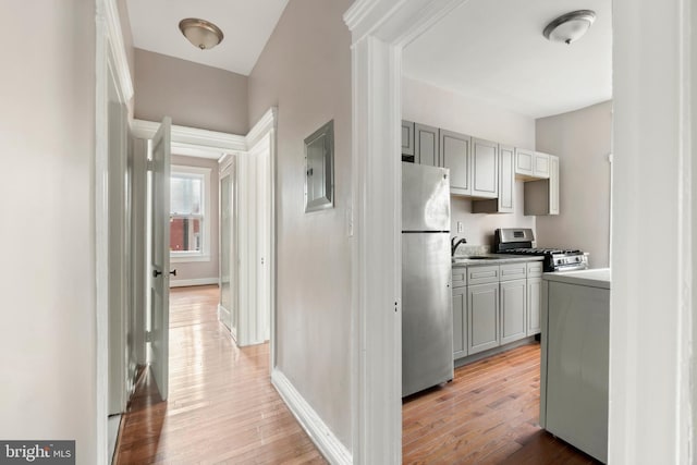corridor featuring baseboards, a sink, electric panel, and light wood-style floors