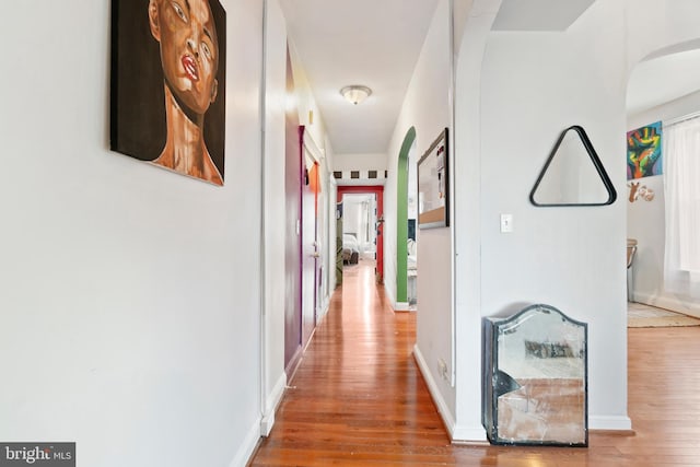 hallway featuring baseboards, arched walkways, and wood finished floors