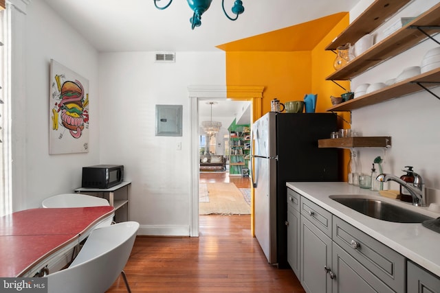 kitchen featuring visible vents, open shelves, freestanding refrigerator, electric panel, and a sink