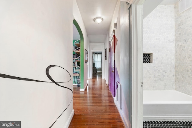 hall with arched walkways, wood finished floors, and visible vents