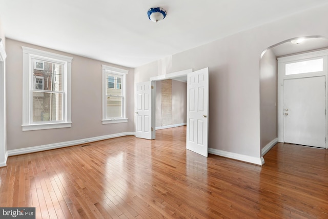 unfurnished room with arched walkways, baseboards, and hardwood / wood-style flooring