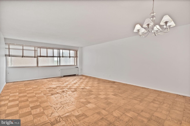 empty room featuring baseboards, a notable chandelier, and radiator heating unit