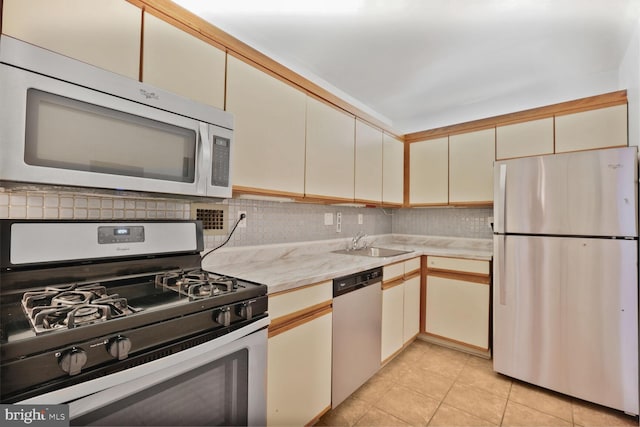kitchen featuring light tile patterned floors, a sink, backsplash, appliances with stainless steel finishes, and cream cabinets