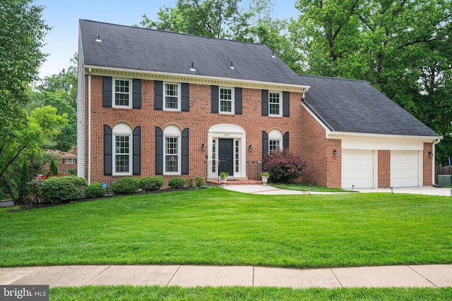 colonial-style house featuring brick siding, an attached garage, a front yard, and concrete driveway