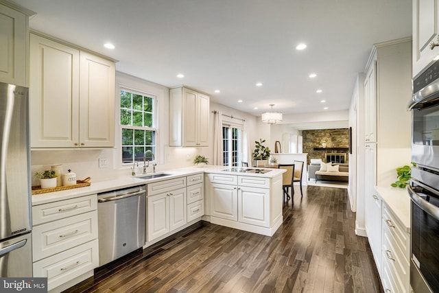 kitchen with stainless steel appliances, a sink, dark wood finished floors, a peninsula, and light countertops