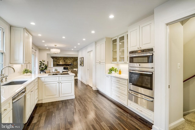 kitchen with a warming drawer, appliances with stainless steel finishes, a sink, a peninsula, and dark wood-style flooring