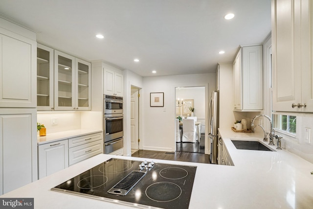 kitchen with stainless steel appliances, a sink, light countertops, recessed lighting, and glass insert cabinets