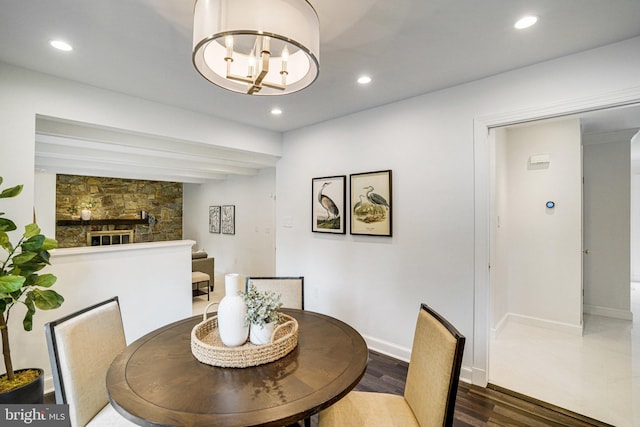 dining space with dark wood-style floors, a chandelier, recessed lighting, a stone fireplace, and baseboards