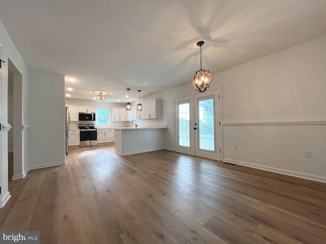 unfurnished living room featuring light wood-type flooring, a sink, baseboards, a notable chandelier, and recessed lighting