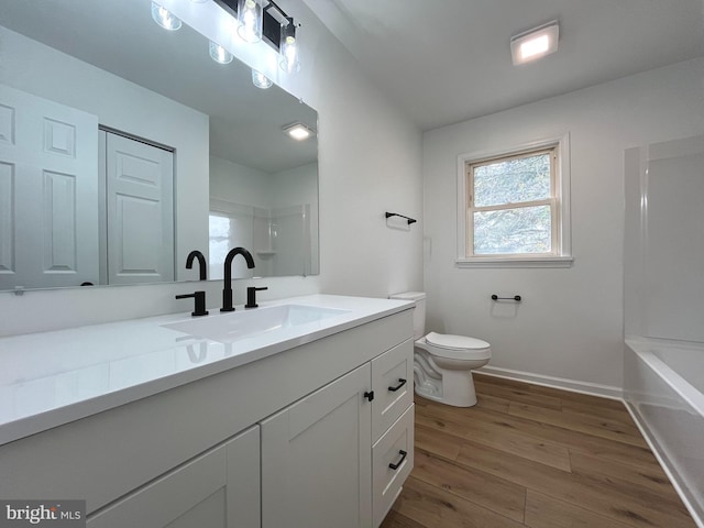 full bath featuring vanity, baseboards, wood finished floors, and toilet