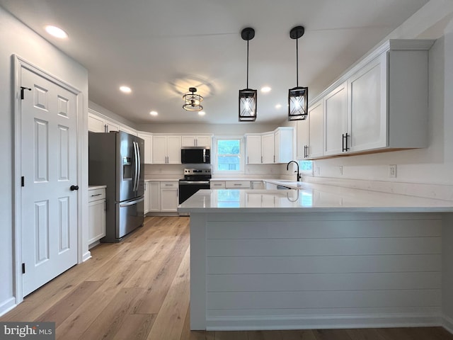 kitchen with a peninsula, white cabinetry, a sink, light wood-style flooring, and appliances with stainless steel finishes