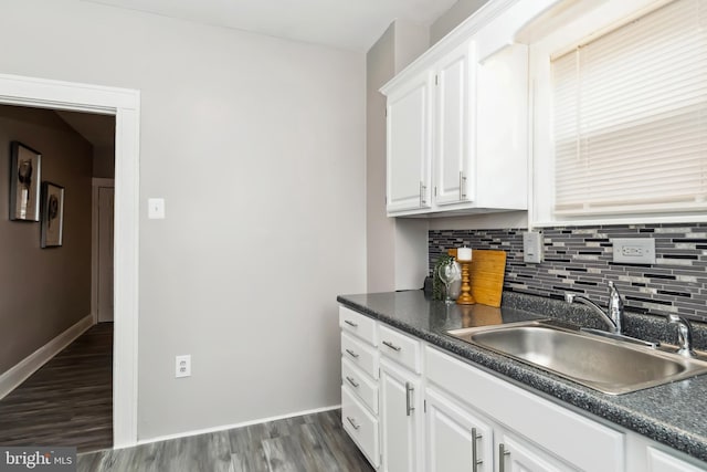 kitchen with dark countertops, tasteful backsplash, a sink, white cabinetry, and dark wood-type flooring