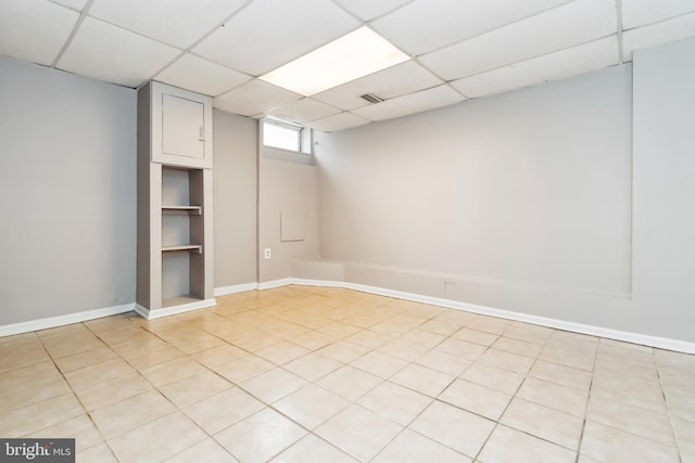 basement featuring baseboards, light tile patterned floors, and a drop ceiling