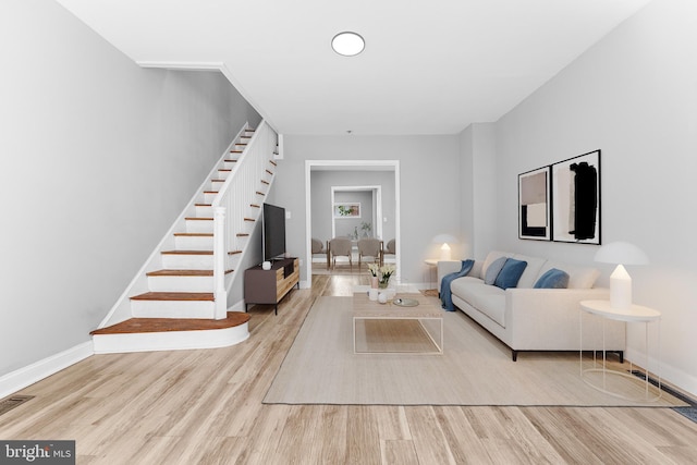 living area with stairway, baseboards, light wood-style floors, and visible vents