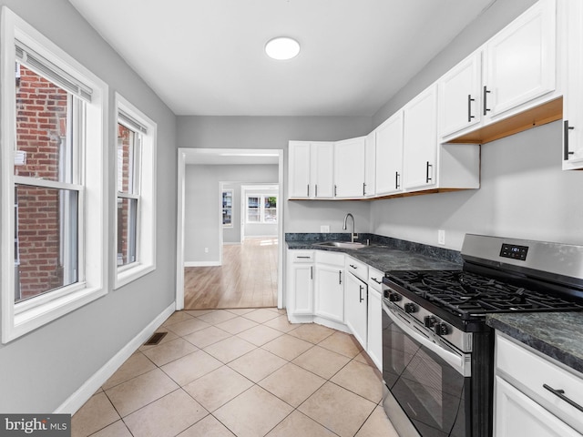kitchen with visible vents, dark countertops, stainless steel gas range oven, white cabinetry, and a sink