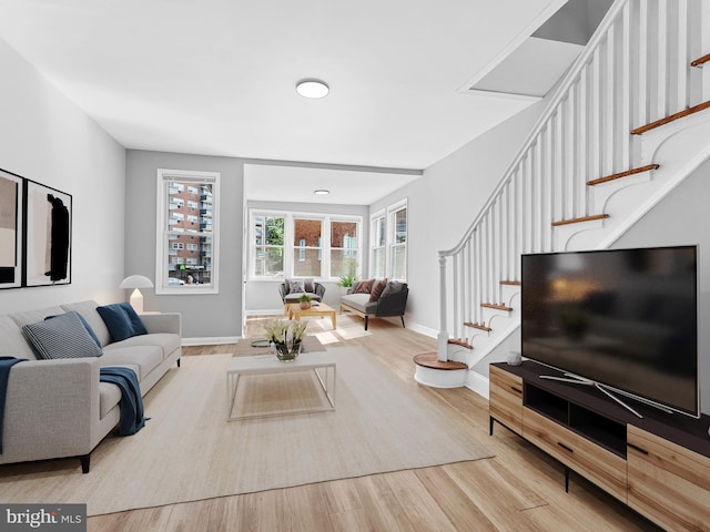living area featuring baseboards, wood finished floors, and stairway