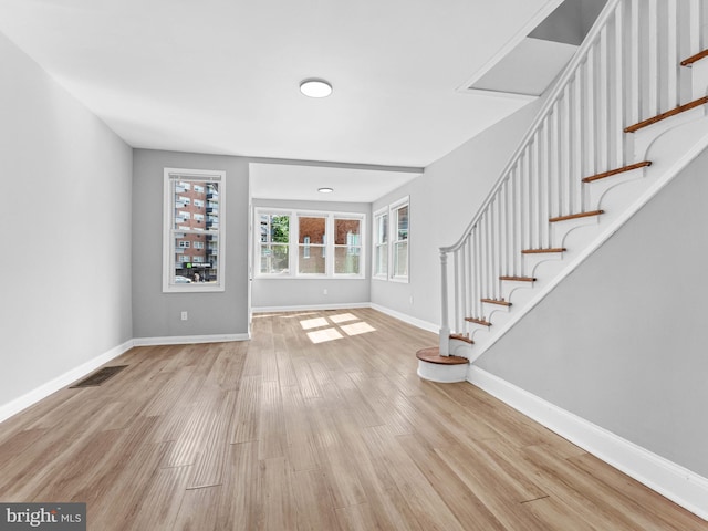 unfurnished living room featuring baseboards, stairs, wood finished floors, and visible vents