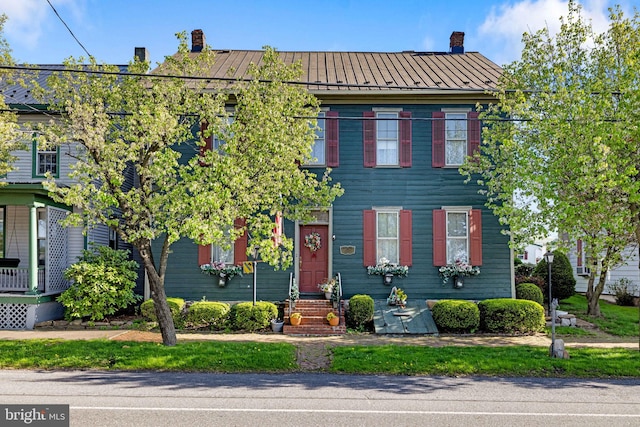 colonial inspired home with entry steps, a chimney, a standing seam roof, and metal roof