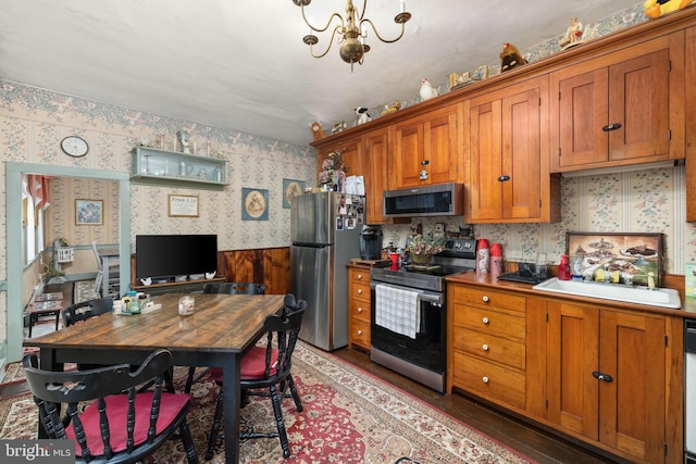 kitchen with a chandelier, wallpapered walls, appliances with stainless steel finishes, and brown cabinetry