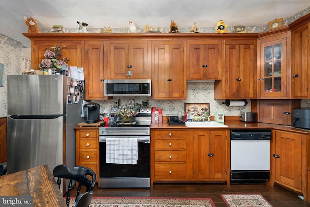kitchen featuring brown cabinetry, a sink, glass insert cabinets, and stainless steel appliances