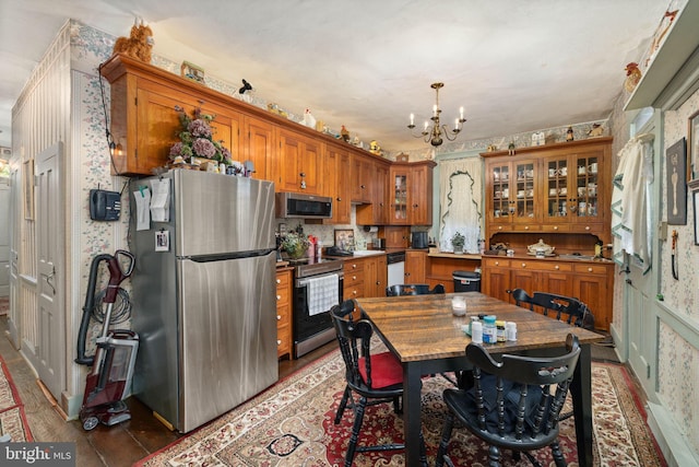 kitchen with glass insert cabinets, brown cabinetry, an inviting chandelier, stainless steel appliances, and wallpapered walls