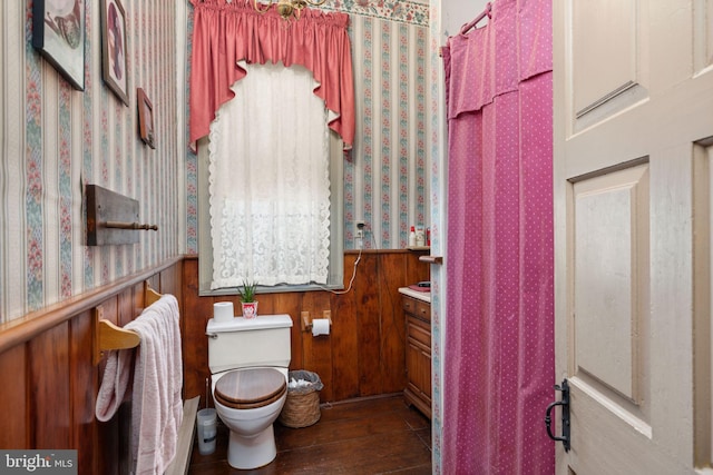 bathroom with wainscoting, wood finished floors, toilet, and wallpapered walls