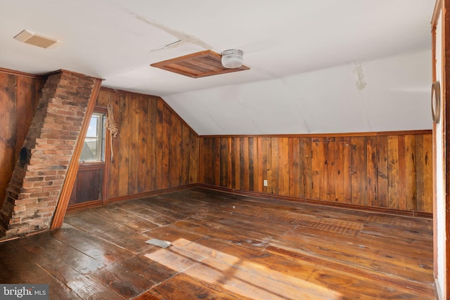 additional living space with visible vents, wood walls, vaulted ceiling, and hardwood / wood-style floors