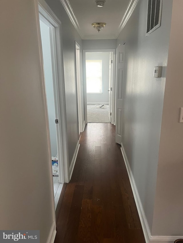 corridor featuring dark wood-type flooring, ornamental molding, and baseboards